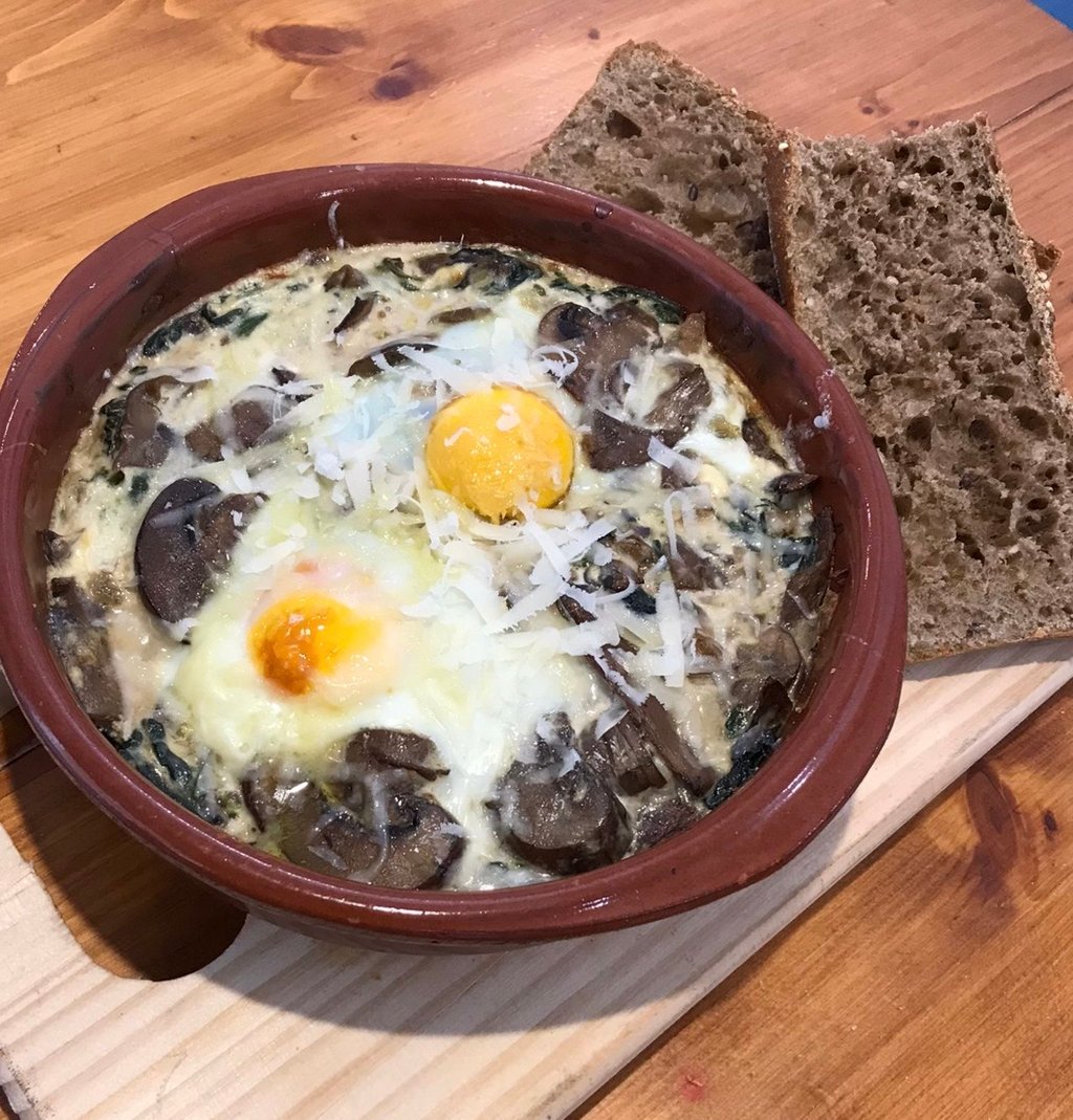 Huevos al horno en setas, espinacas y queso ricotta con grana padano y pan centeno. Añade bacon para 1.50 mas (Tarda 12 min minimo)